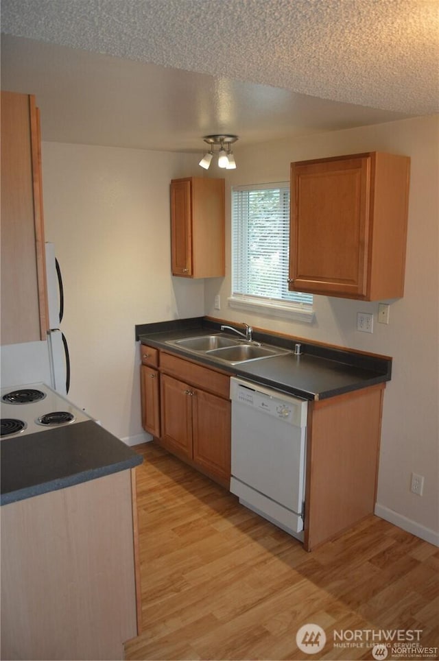 kitchen featuring white appliances, dark countertops, a sink, and light wood-style floors