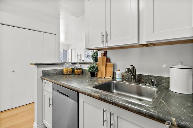 kitchen featuring dark countertops, white cabinetry, dishwasher, and a sink