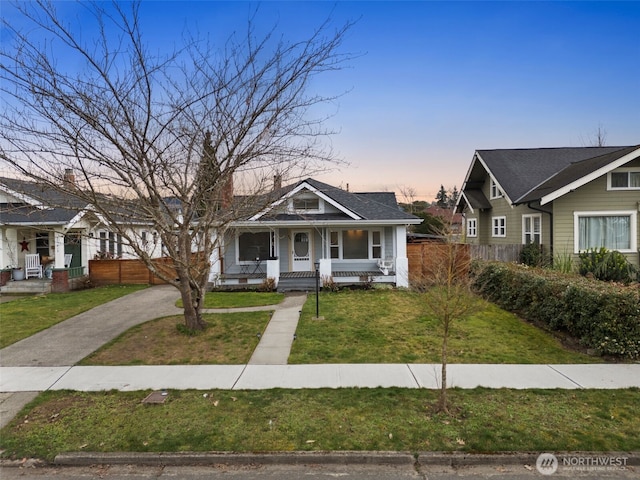 bungalow-style house with driveway, covered porch, fence, and a front yard