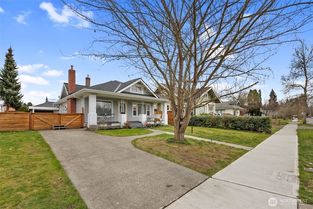 bungalow-style home with covered porch, brick siding, fence, a front lawn, and a chimney