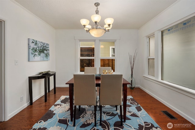 dining room with dark wood-type flooring, visible vents, baseboards, an inviting chandelier, and crown molding