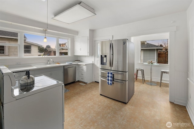 kitchen featuring pendant lighting, light countertops, appliances with stainless steel finishes, a sink, and baseboards