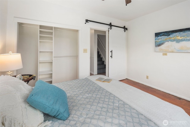 bedroom with a barn door, wood finished floors, a ceiling fan, baseboards, and a closet