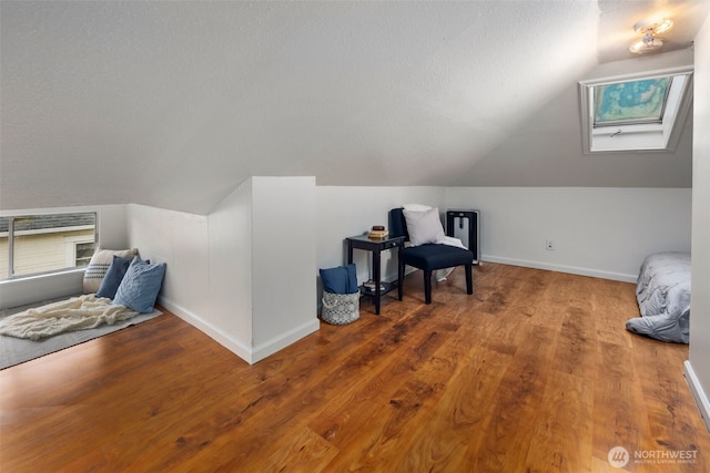 interior space with vaulted ceiling with skylight, a textured ceiling, baseboards, and wood finished floors