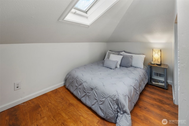 bedroom with vaulted ceiling with skylight, baseboards, and wood finished floors