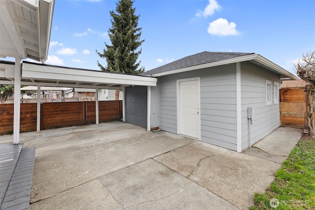 garage featuring concrete driveway, a carport, and fence