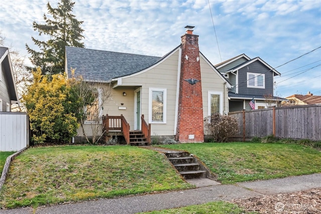 view of front of house featuring a chimney, a shingled roof, a front lawn, and fence