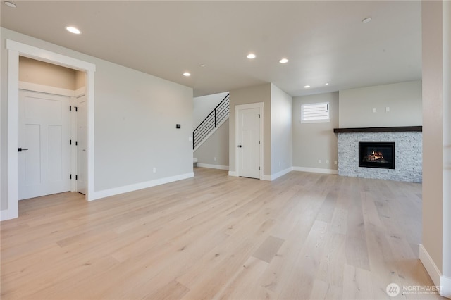 unfurnished living room featuring recessed lighting, a stone fireplace, light wood-type flooring, baseboards, and stairs