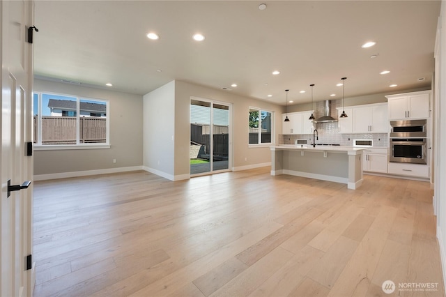 kitchen featuring light wood-style flooring, oven, open floor plan, wall chimney range hood, and backsplash