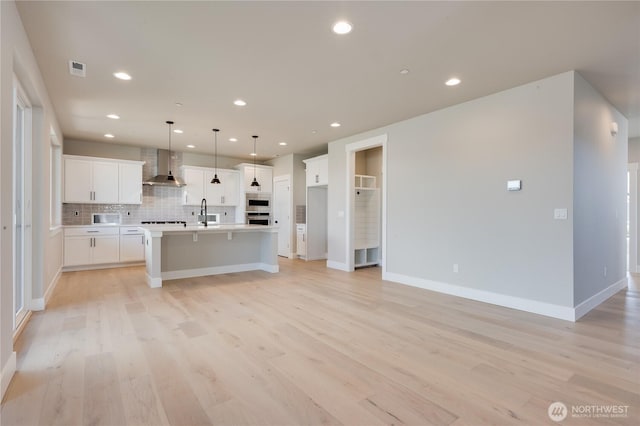 kitchen with decorative backsplash, light wood-style flooring, light countertops, wall chimney range hood, and white cabinetry