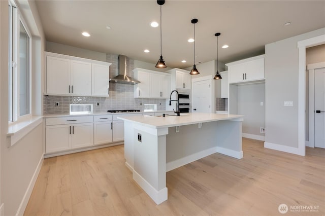 kitchen featuring wall chimney range hood, gas stovetop, white cabinetry, and light wood-style floors