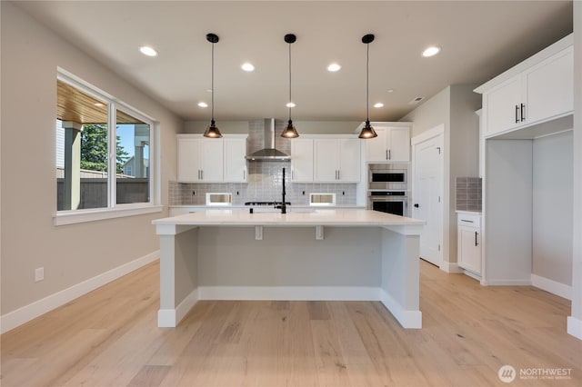 kitchen with wall chimney exhaust hood, light countertops, a center island with sink, and stainless steel appliances