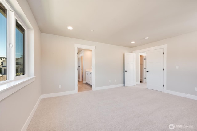 unfurnished bedroom featuring ensuite bath, recessed lighting, baseboards, and light colored carpet