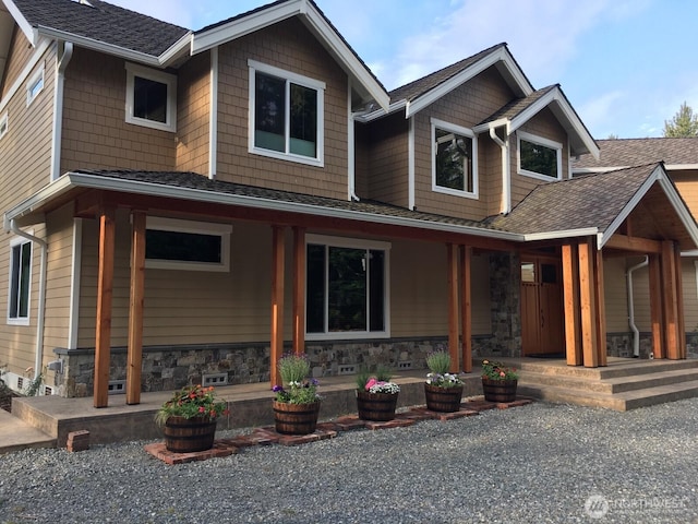 view of front of house with covered porch, stone siding, and roof with shingles