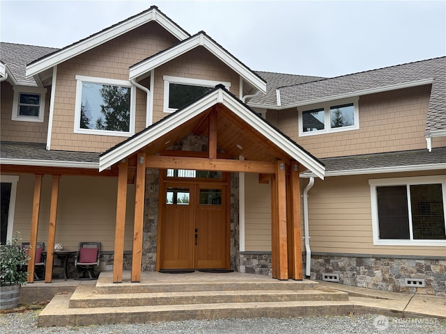 doorway to property featuring stone siding and a shingled roof