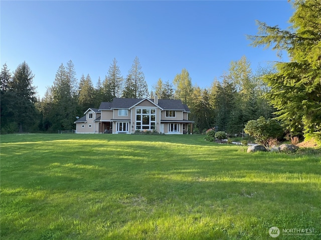 rear view of property with a lawn, a chimney, and a wooded view