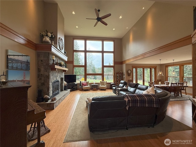 living area featuring ceiling fan, a fireplace, a towering ceiling, and wood finished floors