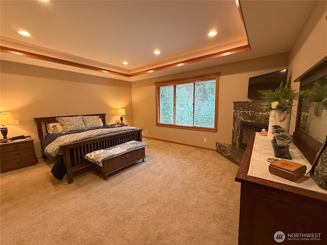 bedroom featuring baseboards, a raised ceiling, light colored carpet, a premium fireplace, and recessed lighting