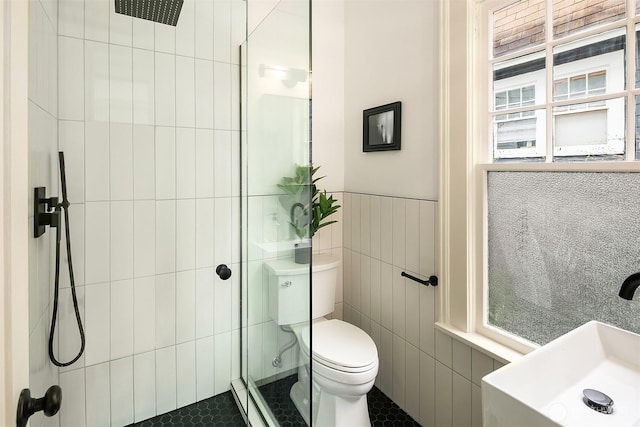 full bathroom featuring a tile shower, a sink, tile walls, toilet, and a wealth of natural light