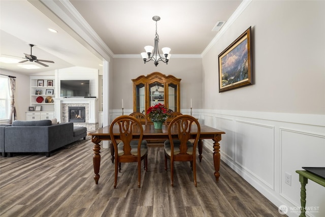 dining area with visible vents, built in features, dark wood-type flooring, crown molding, and a stone fireplace