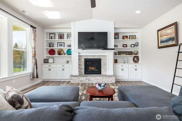 living room with visible vents, baseboards, lofted ceiling, light wood-style flooring, and a stone fireplace