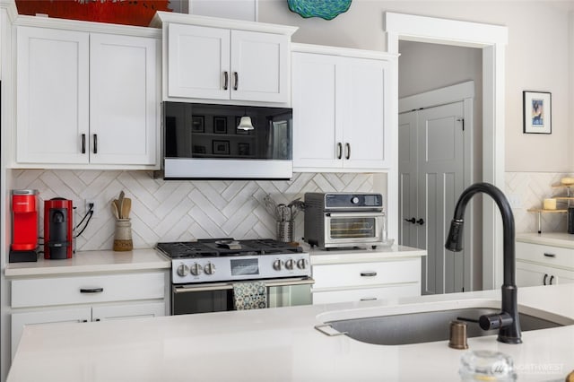 kitchen with a sink, white cabinets, light countertops, decorative backsplash, and gas range