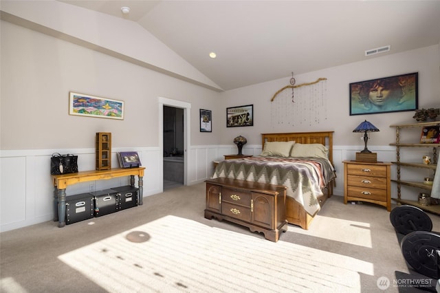 carpeted bedroom with lofted ceiling, a wainscoted wall, and visible vents