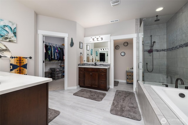 full bath with a relaxing tiled tub, visible vents, a spacious closet, a tile shower, and vanity