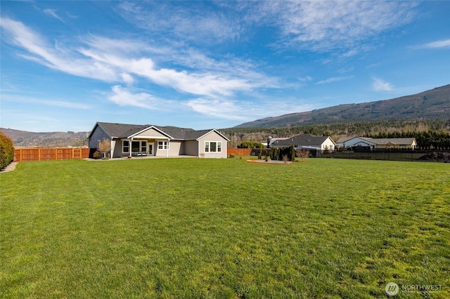 rear view of property with a fenced backyard, a mountain view, and a lawn