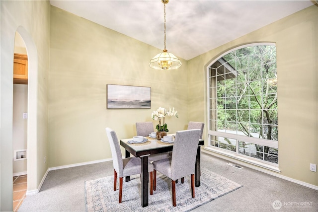 carpeted dining space with arched walkways, visible vents, and baseboards