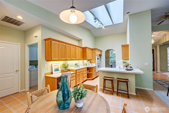 kitchen featuring visible vents, arched walkways, tile counters, and washer and dryer