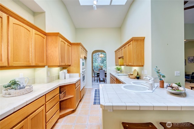 kitchen featuring white appliances, a high ceiling, a skylight, a sink, and tile counters