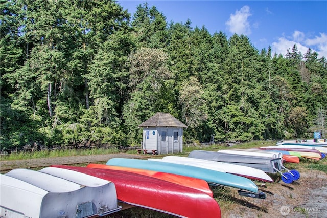 view of swimming pool with a storage shed, a view of trees, and an outbuilding