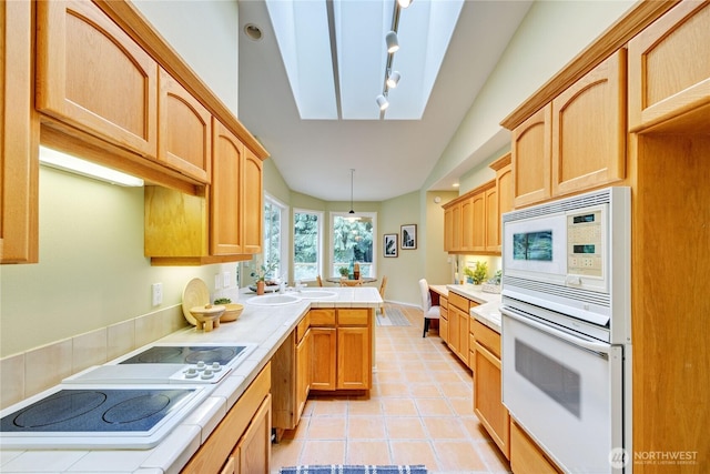 kitchen with vaulted ceiling with skylight, light tile patterned flooring, a peninsula, tile counters, and white electric stovetop