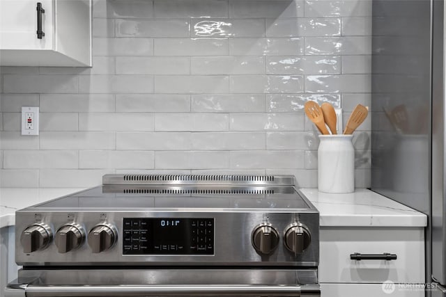 room details with white cabinets, stainless steel range with electric cooktop, backsplash, and light stone countertops