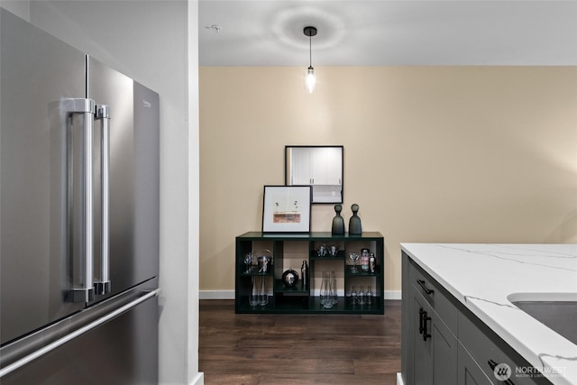 kitchen with dark wood-type flooring, high end refrigerator, light stone counters, and baseboards