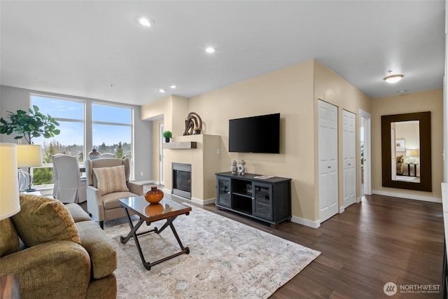 living area with baseboards, dark wood-style flooring, a glass covered fireplace, and recessed lighting