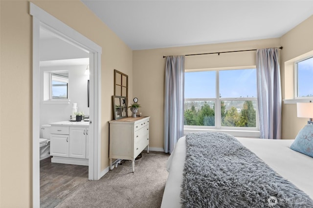 bedroom with multiple windows, baseboards, light colored carpet, and ensuite bathroom