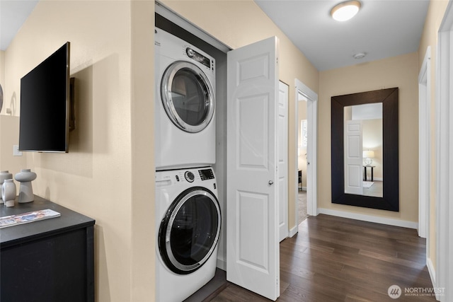 laundry area with laundry area, stacked washer / dryer, dark wood finished floors, and baseboards