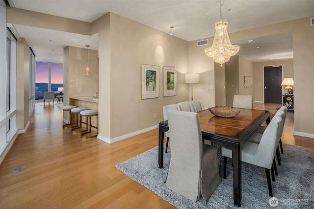 dining area with a chandelier, light wood-type flooring, visible vents, and baseboards