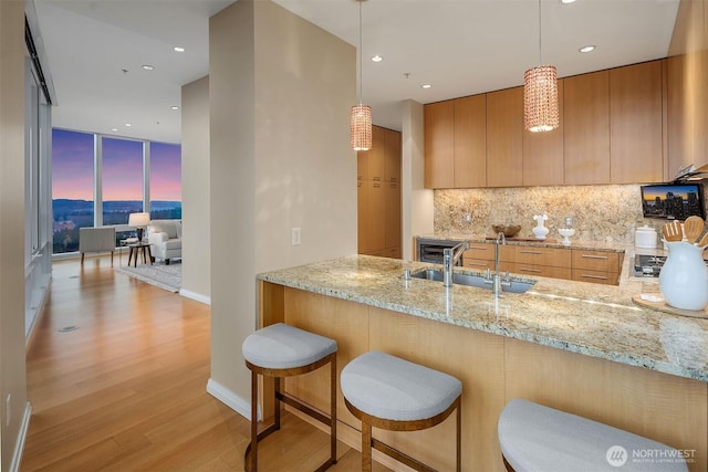 kitchen featuring light stone counters, a sink, decorative backsplash, floor to ceiling windows, and light wood finished floors