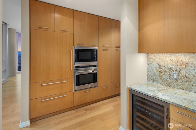 kitchen featuring light wood finished floors, beverage cooler, light stone counters, built in microwave, and stainless steel oven