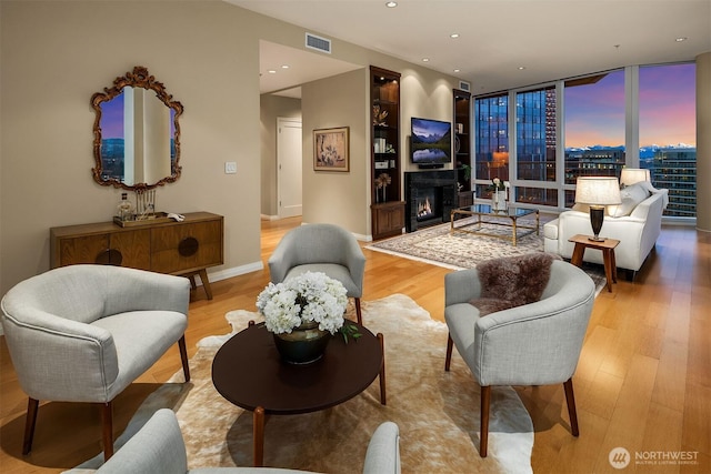 living room with recessed lighting, visible vents, light wood-type flooring, floor to ceiling windows, and a glass covered fireplace