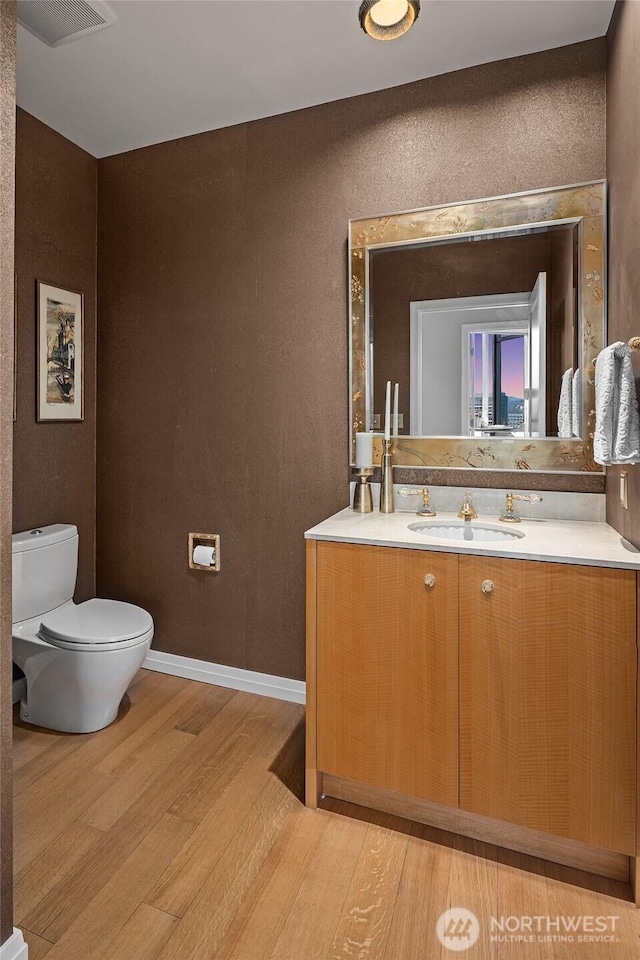 bathroom featuring visible vents, baseboards, toilet, wood finished floors, and vanity