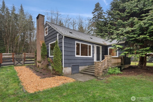 view of front of home with a shingled roof, a front yard, fence, and a chimney