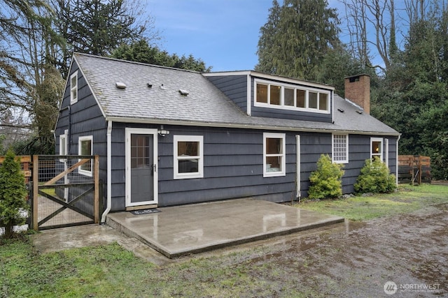 rear view of property with roof with shingles, a chimney, a patio area, and a gate