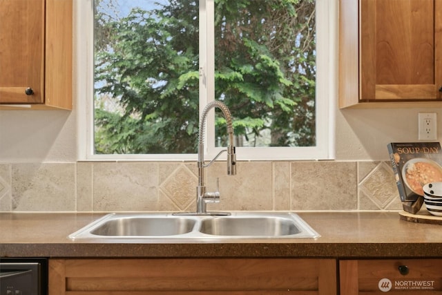 kitchen with a sink, decorative backsplash, brown cabinets, dishwasher, and dark countertops