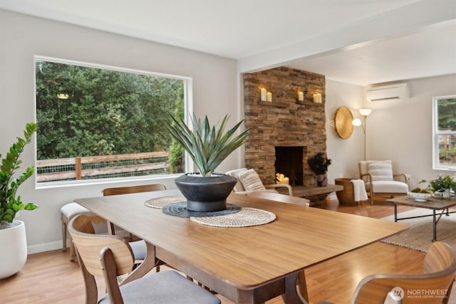 dining room featuring a fireplace, plenty of natural light, light wood finished floors, and a wall mounted AC