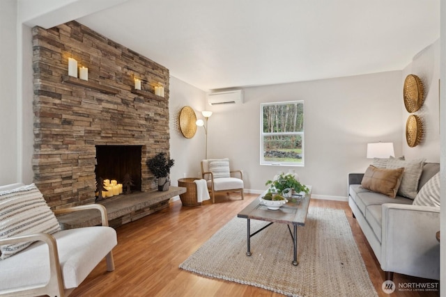 living room featuring a stone fireplace, a wall mounted AC, wood finished floors, and baseboards