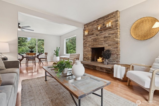 living area with baseboards, a ceiling fan, beamed ceiling, wood finished floors, and a stone fireplace